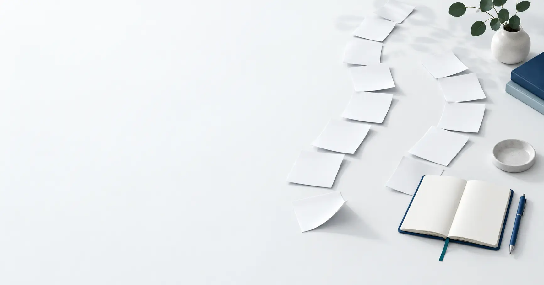 An open notebook and two curved lines of blank paper cards on the right side of a pale desk.