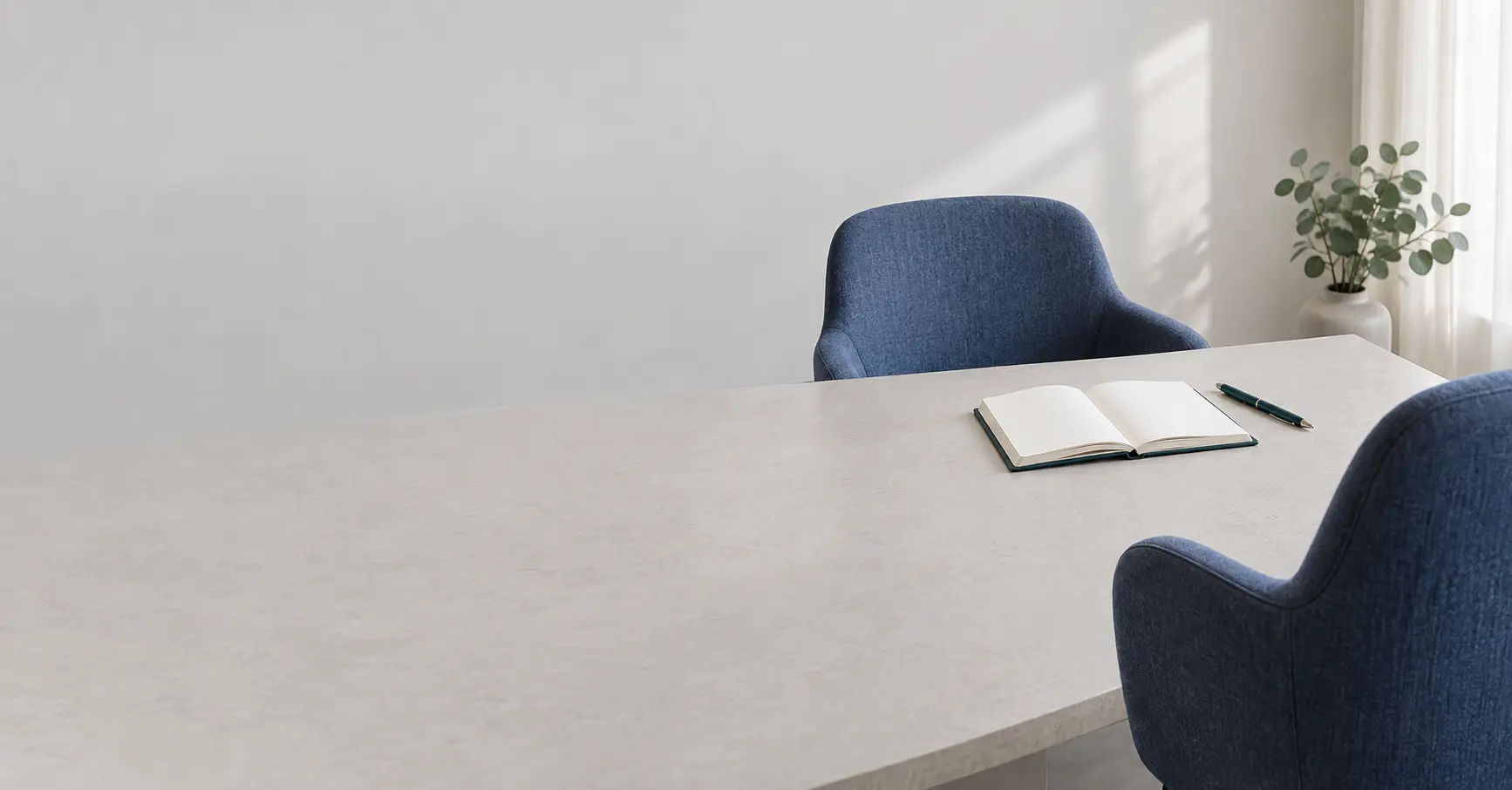 Two blue chairs face a pale table with an open blank notebook and a pen.